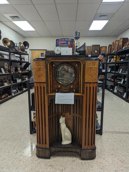 Beautiful restored Zenith Stratosphere console radio (of which there are only ~40 left in existence). There is a white ceramic cat sitting upright in the cutout in front of the speakers.