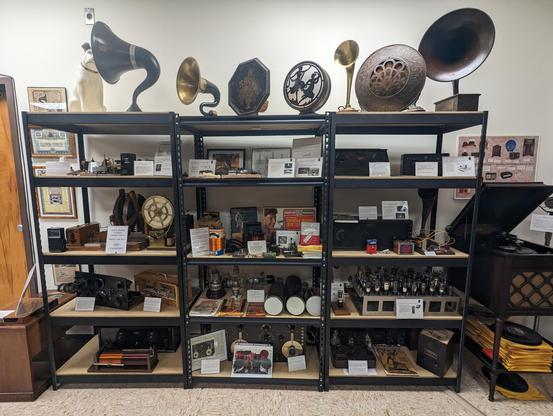 Shelves of older equipment from the beginning of the radio era. Across the top shelves are gramophone horns.