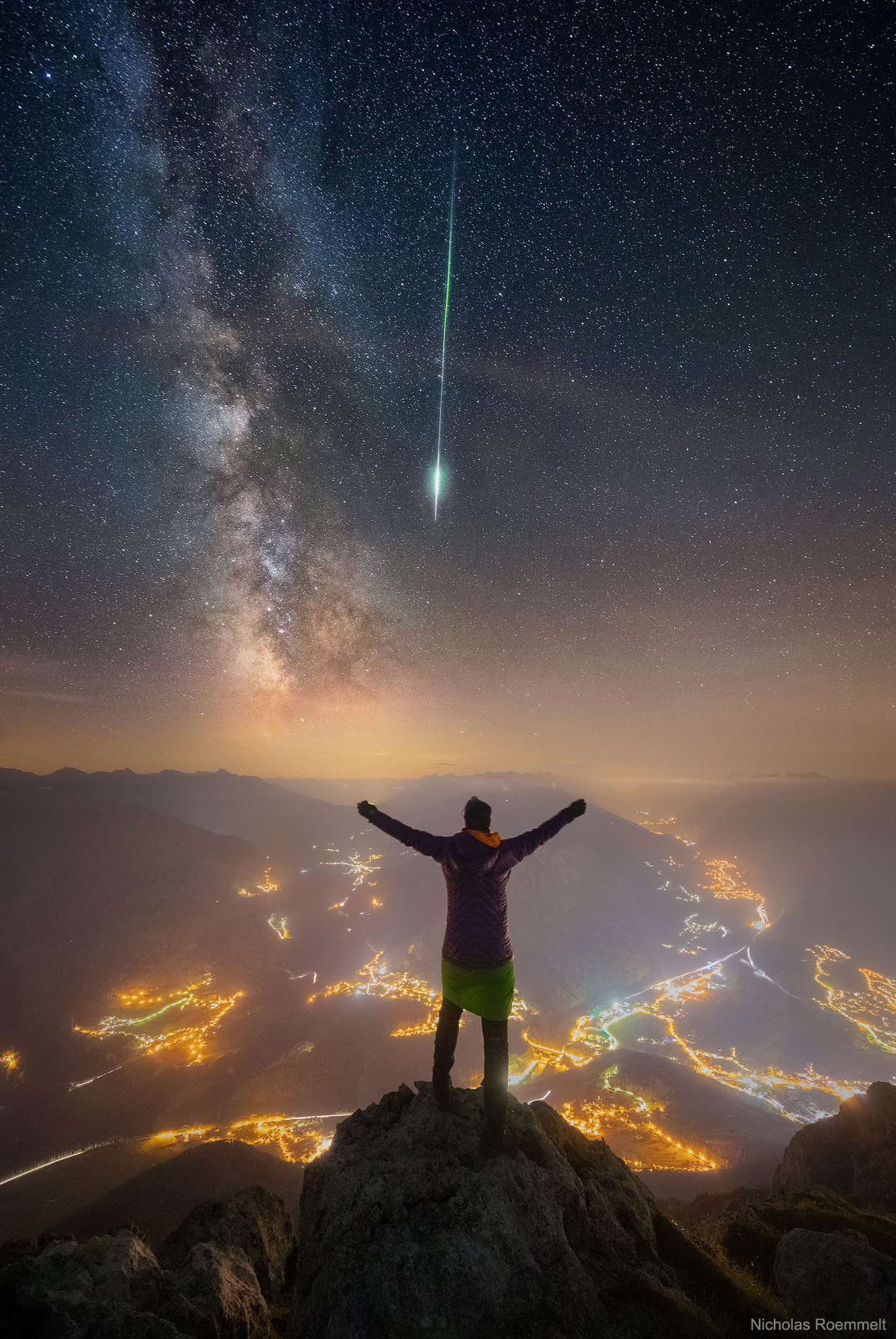 2023 July 16
A person is seen facing away, standing on a peak. Other mountain peaks surround them. City lights are seen in towns and along roads below. Stars in the night sky are above. The band of the Milky Way galaxy slants down from the upper left. A bright green meteor streak slants down from above. 

Meteor and Milky Way over the Alps
 * Image Credit & Copyright: Nicholas Roemmelt (Venture Photography)

Explanation: 
Now this was a view with a thrill. From Mount Tschirgant in the Alps, you can see not only nearby towns and distant Tyrolean peaks, but also, weather permitting, stars, nebulas, and the band of the Milky Way Galaxy. What made the arduous climb worthwhile this night, though, was another peak -- the peak of the 2018 Perseids Meteor Shower. As hoped, dispersing clouds allowed a picturesque sky-gazing session that included many faint meteors, all while a carefully positioned camera took a series of exposures. Suddenly, a thrilling meteor -- bright and colorful -- slashed down right next to the nearly vertical band of the Milky Way. As luck would have it, the camera caught it too. Therefore, a new image in the series was quickly taken with one of the sky-gazers posing on the nearby peak. Later, all of the images were digitally combined. 

Authors & editors: Robert Nemiroff (MTU) & Jerry Bonnell (UMCP)
NASA Official: Phillip Newman Specific rights apply.
